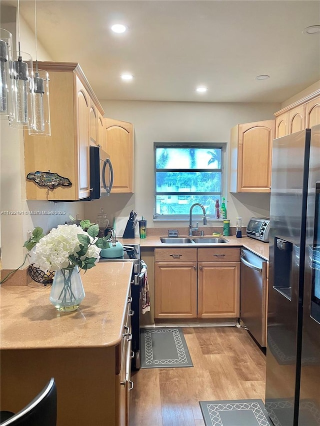 kitchen featuring stainless steel appliances, light brown cabinets, and hanging light fixtures