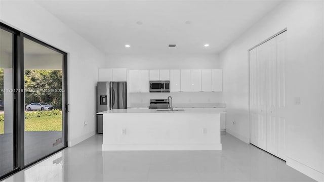 kitchen with a center island with sink, a healthy amount of sunlight, white cabinetry, and stainless steel appliances