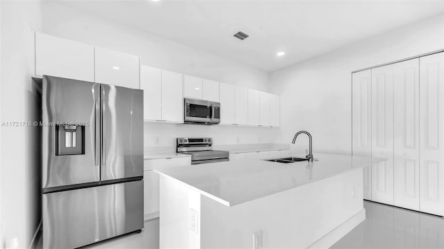 kitchen featuring sink, an island with sink, appliances with stainless steel finishes, light stone counters, and white cabinetry