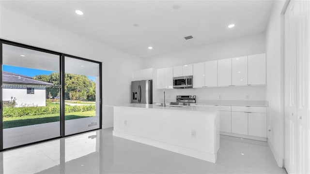 kitchen featuring a kitchen island with sink, sink, light tile patterned floors, appliances with stainless steel finishes, and white cabinetry