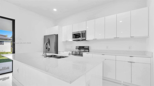 kitchen with light stone countertops, appliances with stainless steel finishes, sink, a center island with sink, and white cabinetry