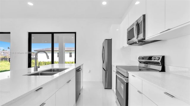 kitchen featuring white cabinets, appliances with stainless steel finishes, light stone counters, and sink