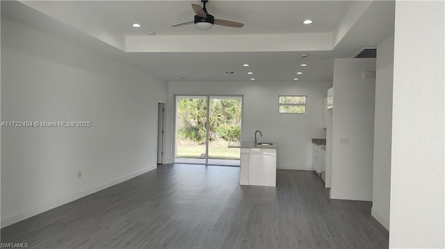 unfurnished living room featuring a raised ceiling, ceiling fan, dark hardwood / wood-style flooring, and sink