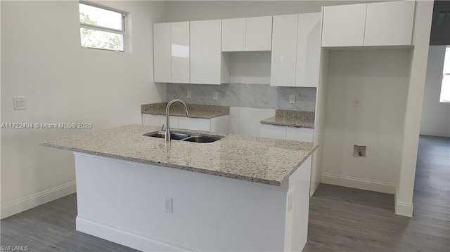 kitchen with light stone countertops, sink, tasteful backsplash, a center island with sink, and white cabinets