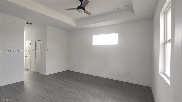 empty room with a tray ceiling, ceiling fan, and dark hardwood / wood-style floors