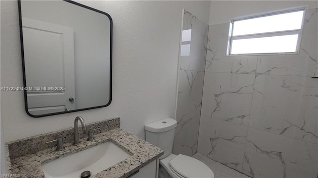 bathroom featuring a tile shower, vanity, and toilet