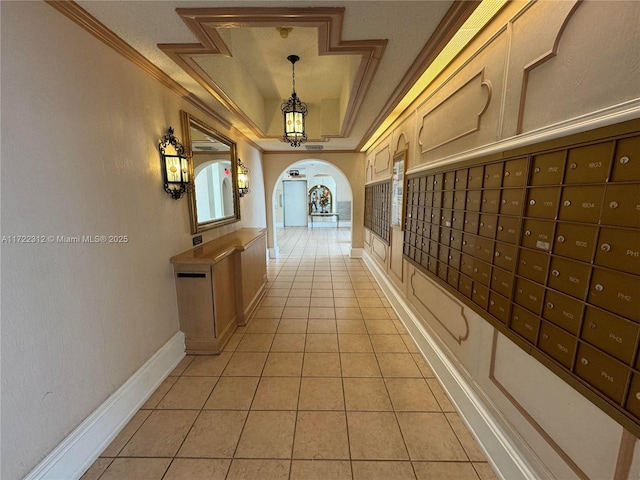 hallway with a raised ceiling, light tile patterned flooring, a mail area, and ornamental molding