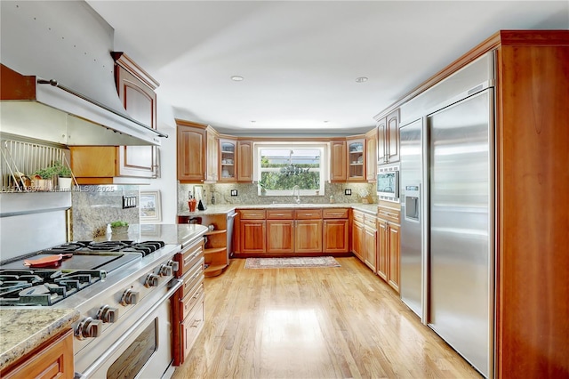 kitchen featuring sink, light stone counters, light hardwood / wood-style flooring, premium range hood, and built in appliances