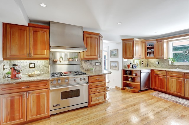 kitchen with light stone countertops, stainless steel appliances, light hardwood / wood-style floors, and wall chimney range hood