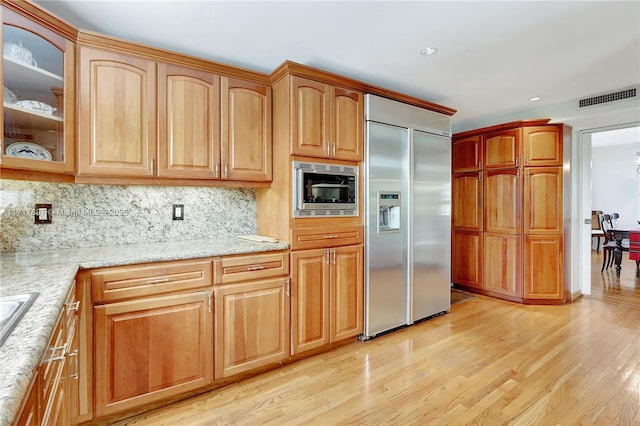 kitchen with built in appliances, light stone countertops, backsplash, and light hardwood / wood-style flooring