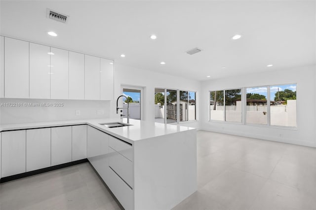 kitchen with kitchen peninsula, light tile patterned floors, white cabinets, and sink