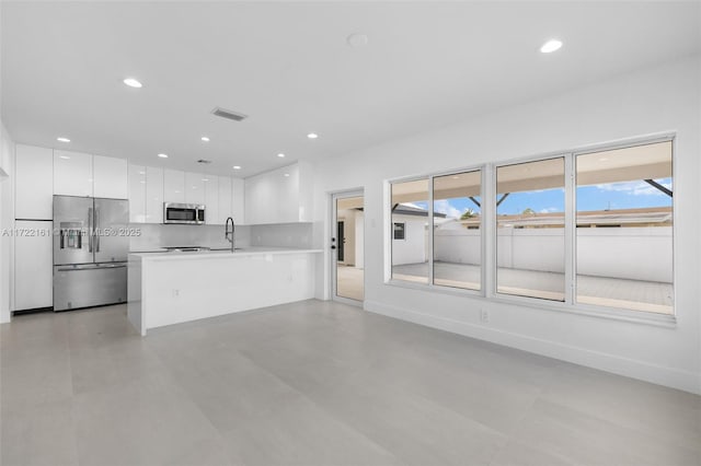 kitchen featuring decorative backsplash, kitchen peninsula, stainless steel appliances, sink, and white cabinets