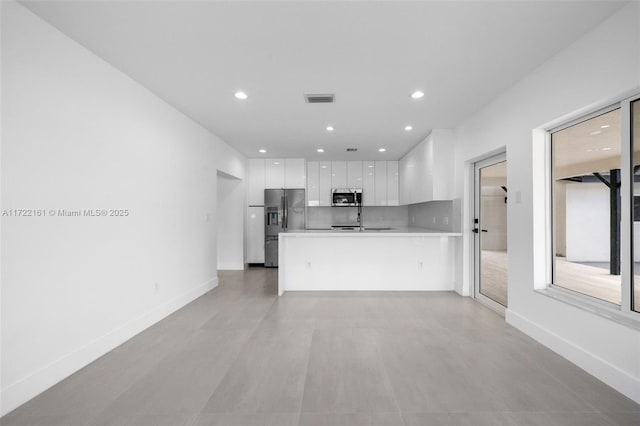 kitchen with white cabinets, decorative backsplash, kitchen peninsula, and appliances with stainless steel finishes