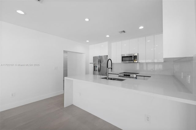 kitchen featuring sink, decorative backsplash, white cabinetry, kitchen peninsula, and stainless steel appliances