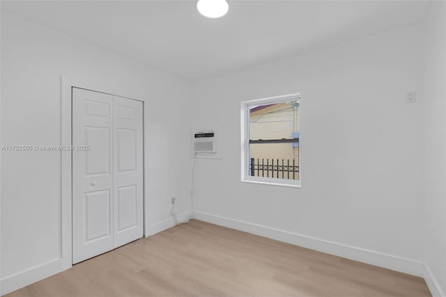 unfurnished bedroom featuring a wall mounted AC, light hardwood / wood-style flooring, and a closet