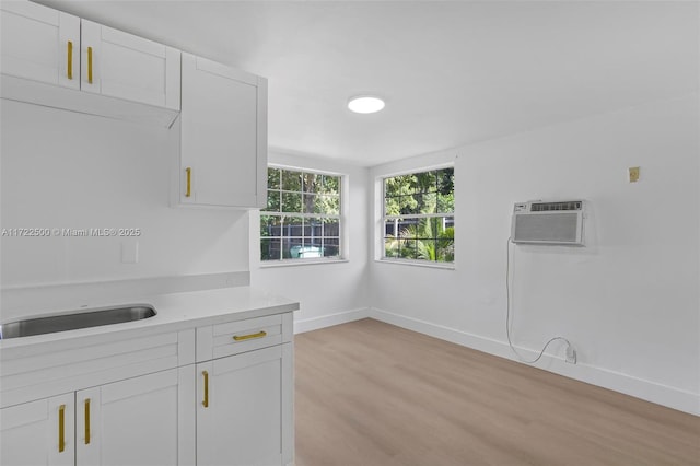 kitchen featuring sink, white cabinets, a wall mounted air conditioner, and light wood-type flooring