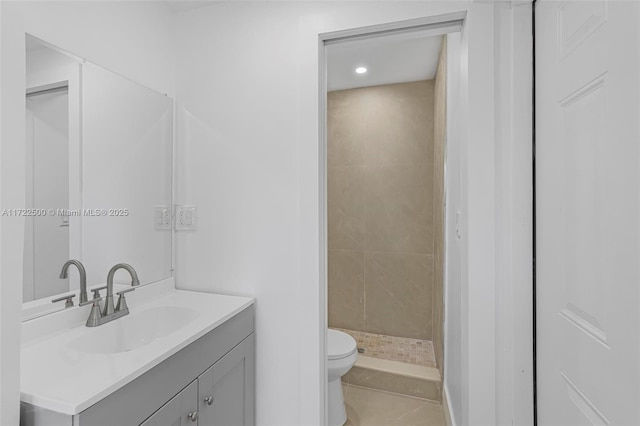 bathroom featuring a tile shower, vanity, toilet, and tile patterned floors