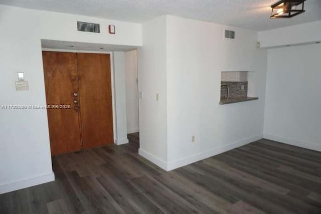 empty room with a textured ceiling, sink, and dark wood-type flooring