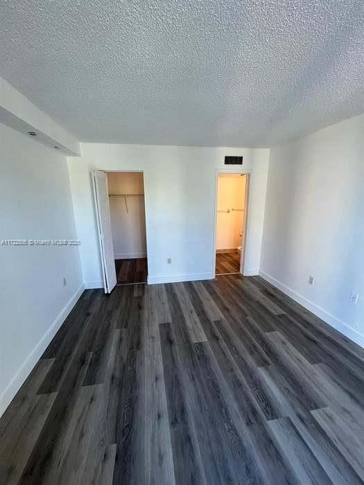 unfurnished room with visible vents, a textured ceiling, dark wood-type flooring, and baseboards
