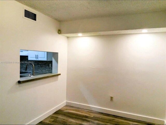 empty room featuring a textured ceiling, visible vents, wood finished floors, a sink, and baseboards