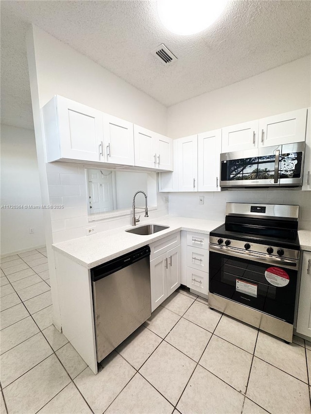 kitchen with sink, light tile patterned flooring, a textured ceiling, white cabinets, and appliances with stainless steel finishes