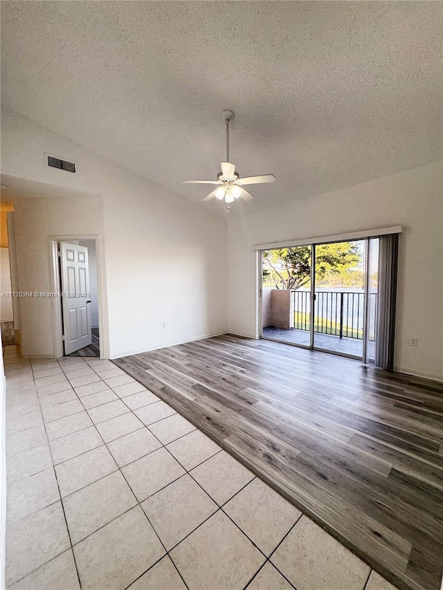 tiled empty room featuring a textured ceiling, ceiling fan, and lofted ceiling