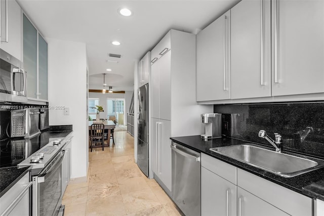 kitchen featuring backsplash, dark stone counters, stainless steel appliances, sink, and white cabinetry