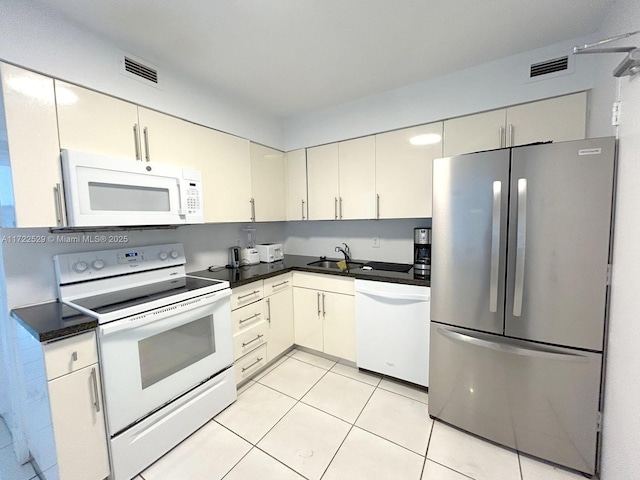 kitchen with white appliances, sink, light tile patterned floors, and cream cabinets