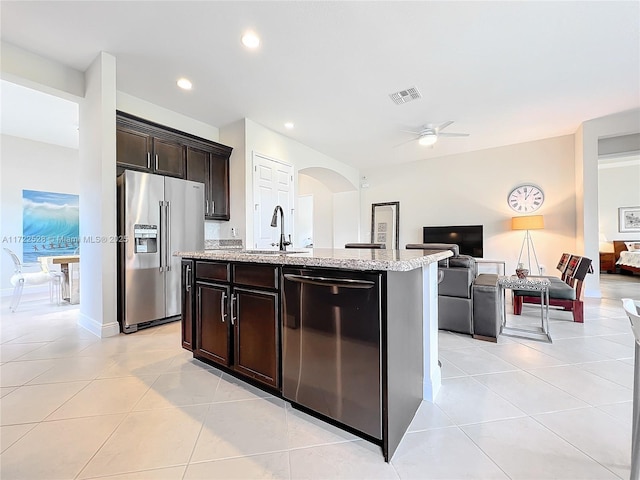 kitchen with high quality fridge, dark brown cabinetry, ceiling fan, a center island with sink, and black dishwasher