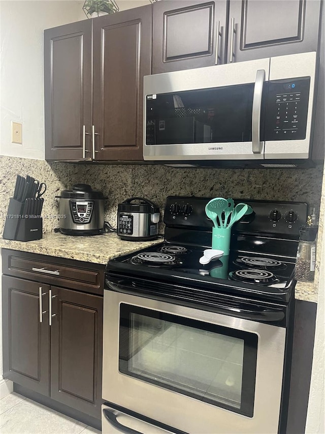 kitchen with decorative backsplash, light stone counters, dark brown cabinetry, stainless steel appliances, and light tile patterned flooring