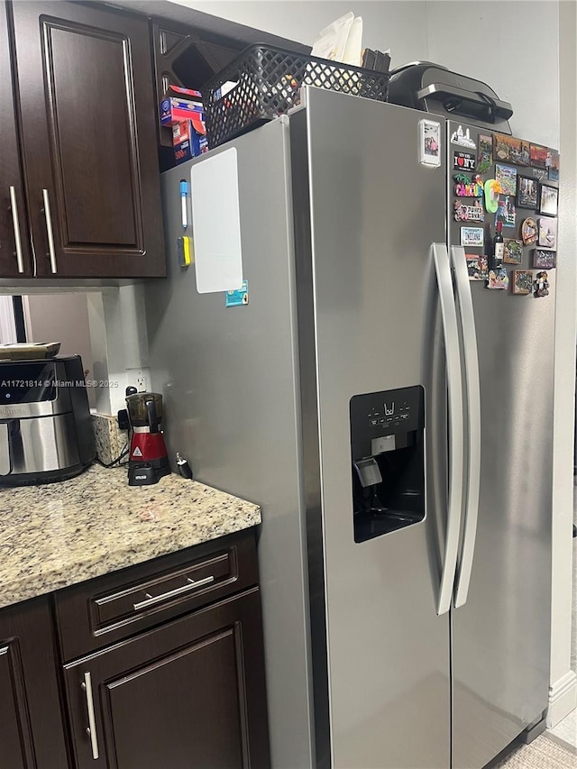 kitchen featuring dark brown cabinetry, stainless steel fridge with ice dispenser, and light stone counters