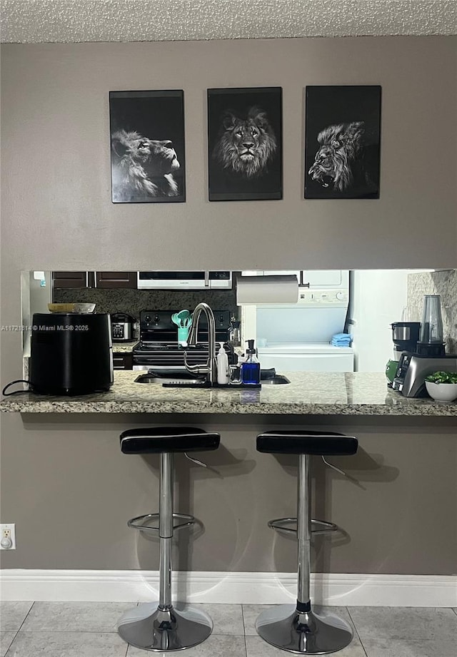 kitchen featuring black range with electric stovetop, sink, a textured ceiling, a breakfast bar, and light tile patterned flooring