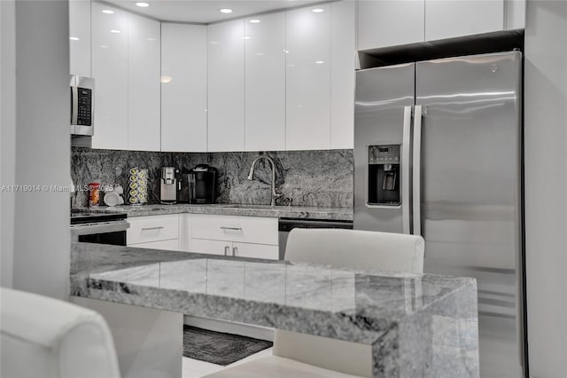 kitchen with appliances with stainless steel finishes, backsplash, white cabinets, light stone counters, and sink