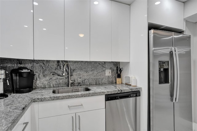 kitchen with light stone countertops, appliances with stainless steel finishes, white cabinets, and sink