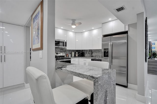 kitchen with light stone countertops, white cabinets, appliances with stainless steel finishes, a kitchen breakfast bar, and ceiling fan