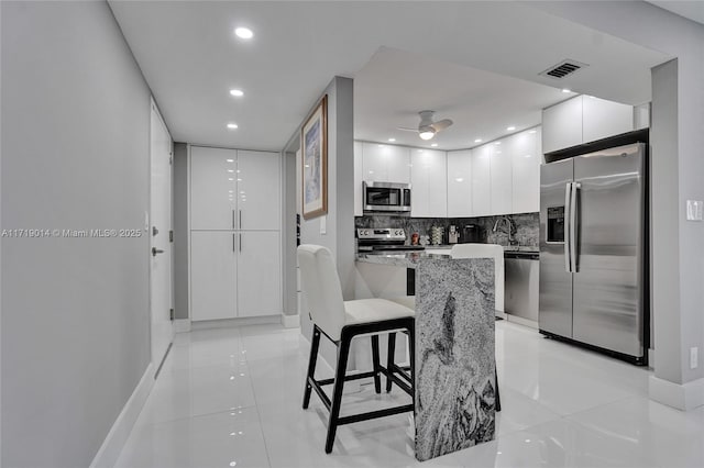 kitchen featuring white cabinets, appliances with stainless steel finishes, decorative backsplash, ceiling fan, and a breakfast bar