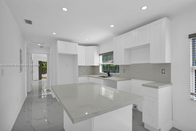 kitchen with sink, a kitchen island, light stone counters, backsplash, and white cabinets