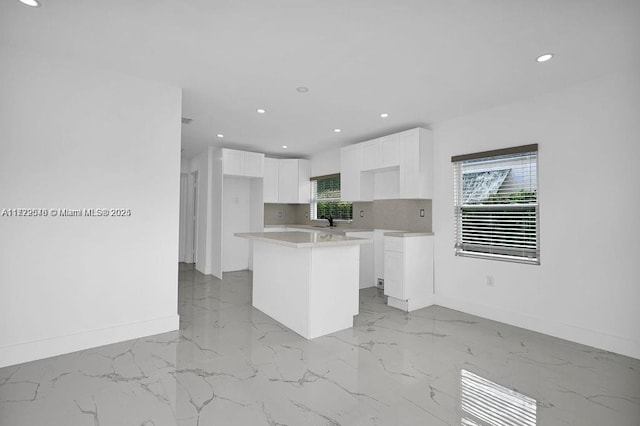 kitchen featuring white cabinets, decorative backsplash, a center island, and sink