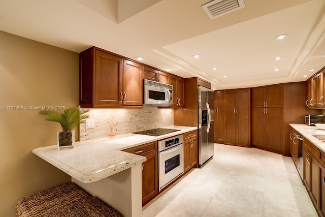 kitchen featuring a breakfast bar area, light stone counters, kitchen peninsula, a tray ceiling, and appliances with stainless steel finishes