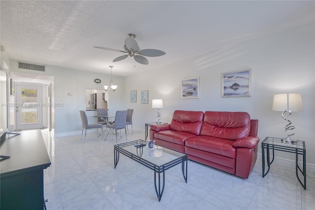 living room with ceiling fan with notable chandelier and a textured ceiling