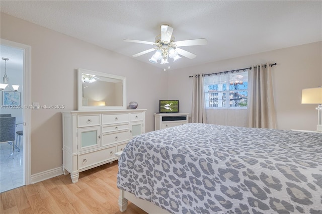 bedroom featuring ceiling fan, ensuite bathroom, a textured ceiling, and light wood-type flooring