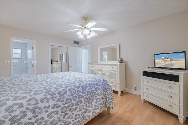 bedroom featuring ceiling fan, light wood-type flooring, a textured ceiling, and ensuite bath