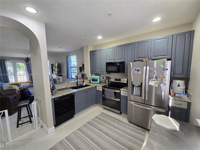 kitchen with sink, gray cabinets, light stone counters, and black appliances