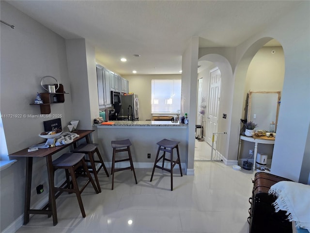 kitchen featuring a kitchen bar, kitchen peninsula, light stone countertops, and stainless steel refrigerator