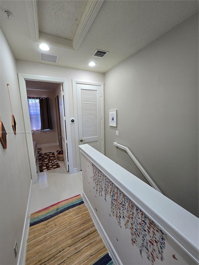 hallway featuring a tray ceiling, crown molding, and a textured ceiling