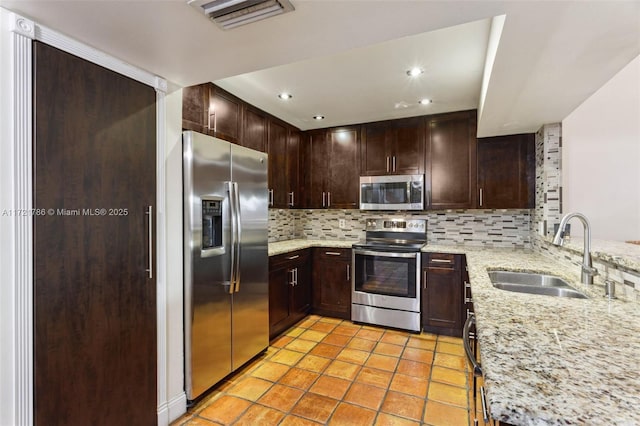 kitchen with appliances with stainless steel finishes, tasteful backsplash, light stone counters, and sink