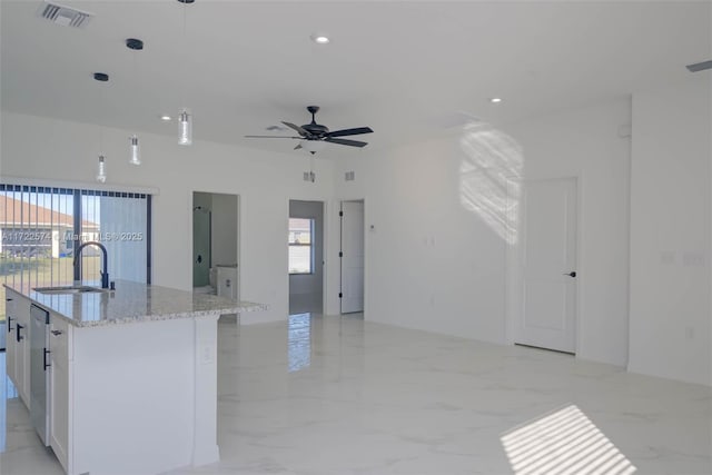 kitchen with a kitchen island with sink, sink, hanging light fixtures, light stone counters, and white cabinetry