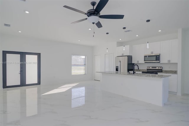 kitchen with light stone countertops, hanging light fixtures, an island with sink, white cabinets, and appliances with stainless steel finishes