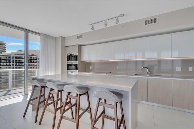 kitchen with tasteful backsplash, expansive windows, double oven, sink, and light tile patterned floors