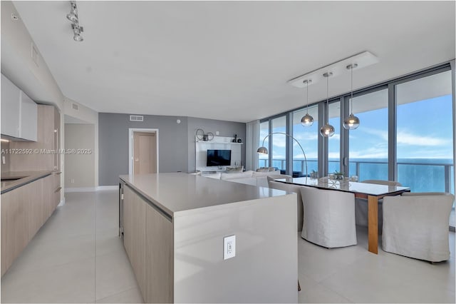 kitchen featuring pendant lighting, expansive windows, light tile patterned floors, light brown cabinetry, and a kitchen island